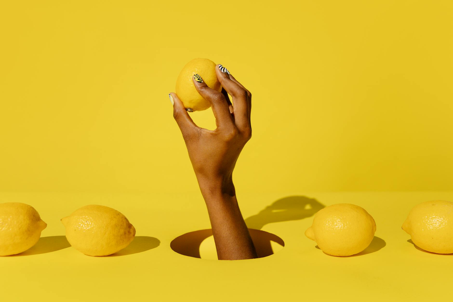 A hand holding a fresh lemon against a bright yellow background, representing renewed vitality and healing.