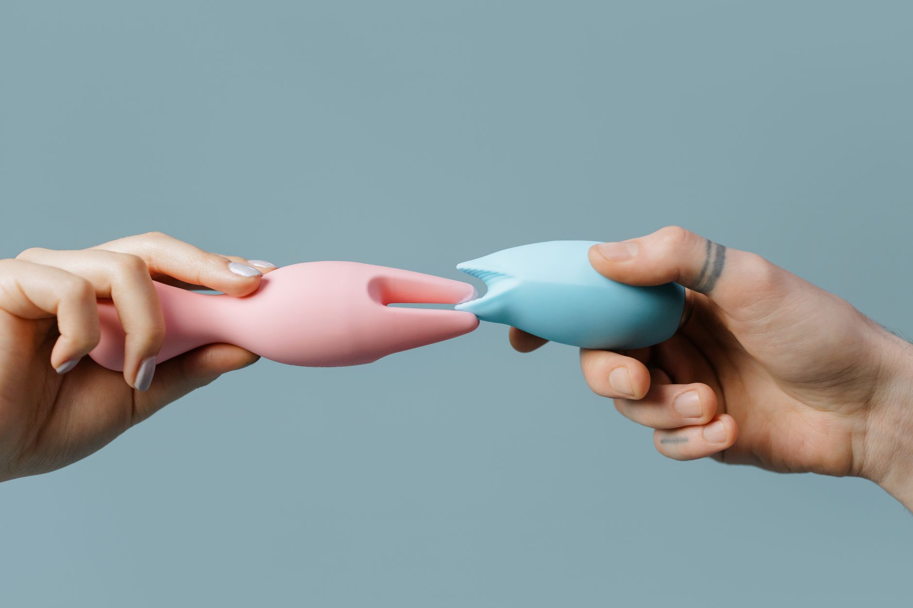 Hand holding a pink clitoral vibrator with art books in soft focus behind it